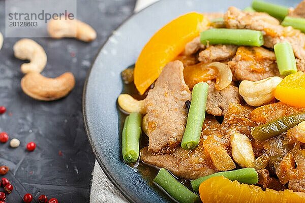 Gebratenes Schweinefleisch mit Pfirsichen  Cashewkernen und grünen Bohnen auf einem schwarzen Betonhintergrund. Draufsicht  Nahaufnahme  chinesische Küche  selektiver Fokus  Makro