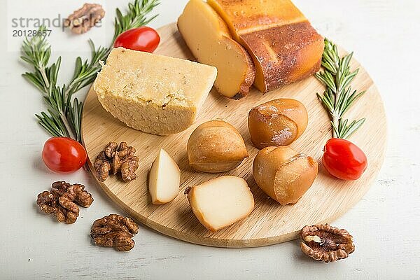 Geräucherter Käse und verschiedene Käsesorten mit Rosmarin und Tomaten auf einem Holzbrett auf einem weißen Holzhintergrund. Seitenansicht  Nahaufnahme  selektiver Fokus