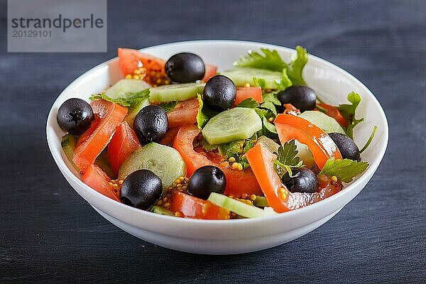 Vegetarischer Salat aus Tomaten  Gurken  Petersilie  Oliven und Senf auf schwarzem Holzuntergrund  Nahaufnahme  selektiver Fokus