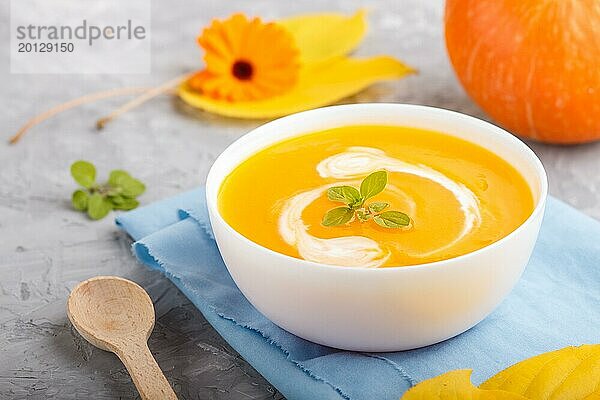 Traditionelle Kürbiscremesuppe in weißer Schale auf grauem Betonhintergrund mit blauer Serviette. Seitenansicht  Nahaufnahme  selektiver Fokus