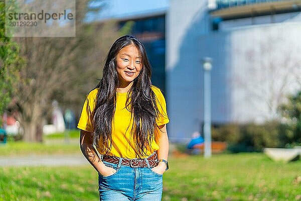 Porträt einer jungen asiatischen Frau steht auf einem College Campus und lächelt in die Kamera