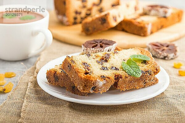 Hausgemachter Kuchen mit Rosinen  getrockneten Kaki und einer Tasse heißer Schokolade auf einem grauen Betonhintergrund und Leinenstoff. Seitenansicht  Nahaufnahme  selektiver Fokus