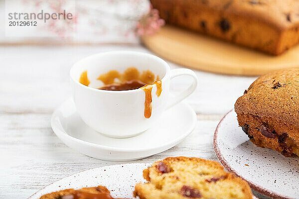 Hausgemachter Kuchen mit Rosinen  Mandeln  weichem Karamell und einer Tasse Kaffee auf einem weißen Holzhintergrund. Seitenansicht  Nahaufnahme  selektiver Fokus