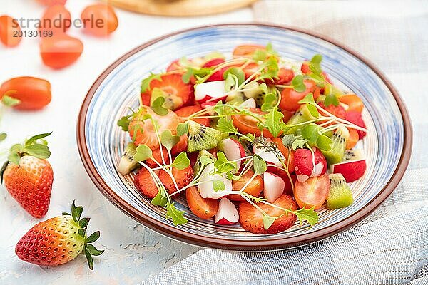 Vegetarischer Obst und Gemüsesalat aus Erdbeeren  Kiwi  Tomaten  Mikrogrünsprossen auf weißem Betonhintergrund und Leinentextil. Seitenansicht  Nahaufnahme  selektiver Fokus