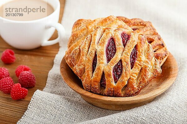 Blätterteigbrötchen mit Erdbeermarmelade auf hölzernem Hintergrund mit Leinentuch und einer Tasse Kaffee. Seitenansicht  Nahaufnahme  selektiver Fokus