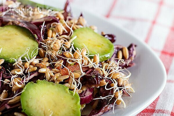 Vegetarischer Salat aus Purpurkohl  gekeimtem Weizen  Tomaten und Avocado auf Leinentischdecke  Nahaufnahme  selektiver Fokus