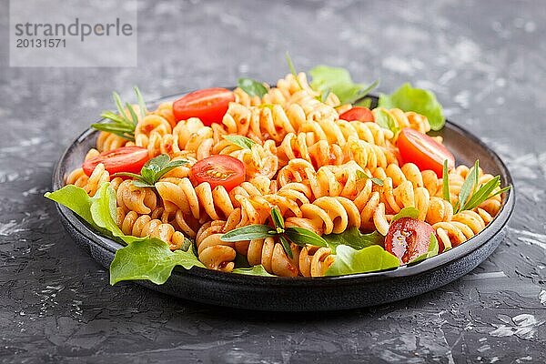 Fusilli Nudeln mit Tomatensauce  Kirschtomaten  Salat und Kräutern auf einem schwarzen Betonhintergrund. Seitenansicht  Nahaufnahme