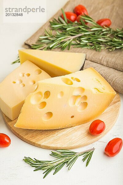 Verschiedene Käsesorten mit Rosmarin und Tomaten auf einem Holzbrett auf einem weißen Holzhintergrund und Leinenstoff. Seitenansicht  Nahaufnahme  selektiver Fokus