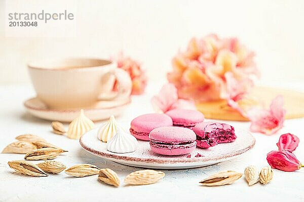 Lila Makronen oder Makronen Kuchen mit Tasse Kaffee auf einem weißen Beton Hintergrund mit Blumen verziert. Seitenansicht  Nahaufnahme  selektiver Fokus