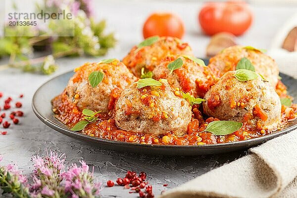 Schweinefleischbällchen mit Tomatensauce  Oreganoblättern  Gewürzen und Kräutern auf blauem Keramikteller auf grauem Betonhintergrund mit Leinentextil. Seitenansicht  Nahaufnahme  selektiver Fokus