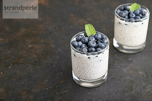 Joghurt mit Heidelbeeren und Chia im Glas auf schwarzem Betonhintergrund. Seitenansicht  Nahaufnahme  Kopierraum