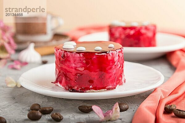 Roter Kuchen mit Soufflé Creme und Tasse Kaffee auf grauem Betonhintergrund und rotem Textil. Seitenansicht  Nahaufnahme. selektiver Fokus