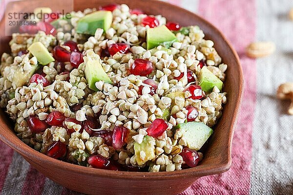 Salat aus gekeimtem Buchweizen  Avocado  Walnuss und Granatapfelkernen in einem Tonteller auf weißem Holzuntergrund. Seitenansicht  Nahaufnahme  selektiver Fokus