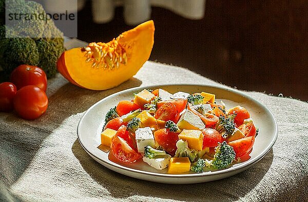 Vegetarischer Salat mit Brokkoli  Tomaten  Fetakäse und Kürbis auf weißem Keramikteller auf Leinenstoff  Seitenansicht  Nahaufnahme  selektiver Fokus  natürliches Tageslicht