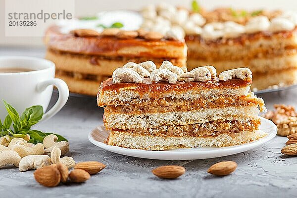 Stück hausgemachter Kuchen mit Karamellcreme und Nüssen mit einer Tasse Kaffee auf einem grauen Betonhintergrund. Seitenansicht  Nahaufnahme  selektiver Fokus