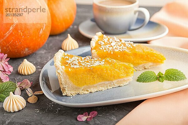 Zwei Stücke traditioneller amerikanischer Kürbiskuchen mit einer Tasse Kaffee auf einem schwarzen Betonhintergrund und orangefarbenem Textil. Seitenansicht  Nahaufnahme  Kontrast  selektiver Fokus