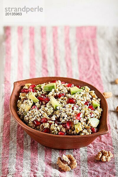 Salat aus gekeimtem Buchweizen  Avocado  Walnuss und Granatapfelkernen in einem Tonteller auf weißem Holzhintergrund. Seitenansicht  Kopierraum  selektiver Fokus