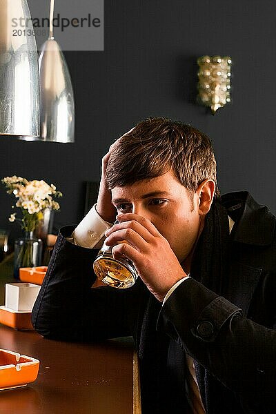 Junger Mann im Anzug sitzt an einer Bar und trinkt Alkohol