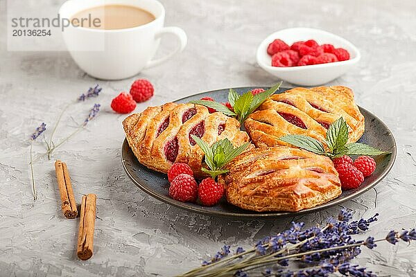 Blätterteigbrötchen mit Erdbeermarmelade auf blauem Keramikteller auf grauem Betonhintergrund  Tasse Kaffee  Lavendel  Zimt  Minzblätter. Seitenansicht  Nahaufnahme  selektiver Fokus