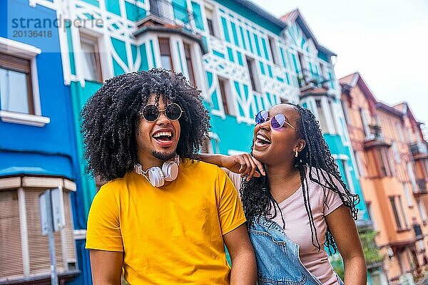 Glückliche afrikanische coole Freunde mit Sonnenbrillen und Jeans lässige Kleidung lachen und plaudern in einer bunten Straße