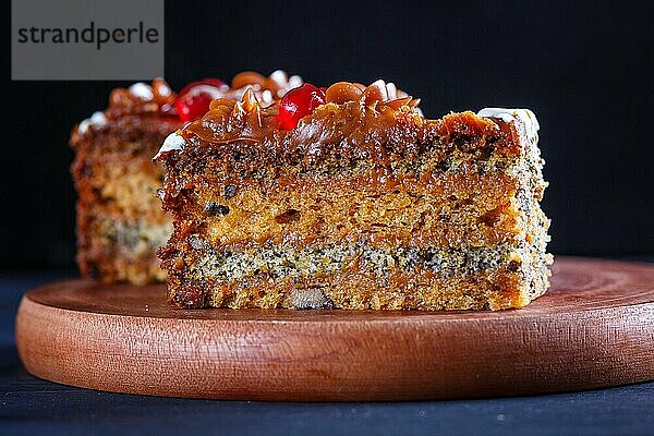 Ein Stück Kuchen mit Karamellcreme und Mohn auf einem hölzernen Küchenbrett. Nahaufnahme  selektiver Fokus  schwarzer Hintergrund