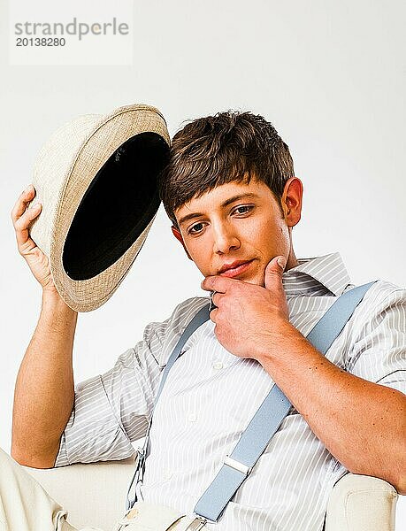 Junger Mann mit Hut und Hosenträgern in einem Sessel sitzend