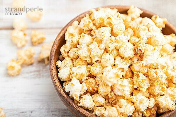 Popcorn mit Karamell in einer Holzschüssel und eine Tasse Kaffee auf einem weißen Holzhintergrund und Leinenstoff. Seitenansicht  Nahaufnahme  selektiver Fokus