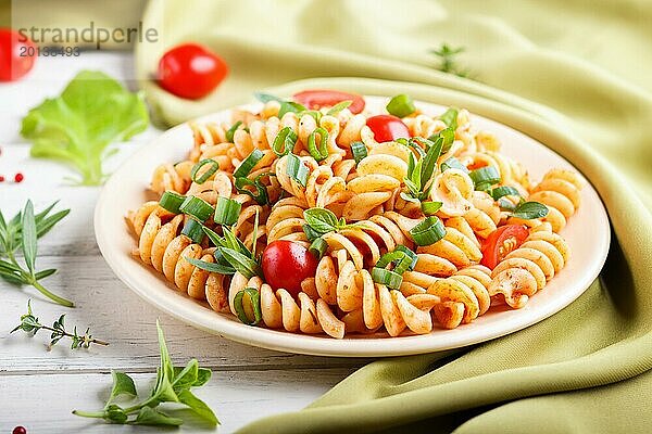 Fusilli Nudeln mit Tomatensauce  Kirschtomaten  Salat und Kräutern auf weißem Holzhintergrund mit grünem Textil. Seitenansicht  Nahaufnahme  selektiver Fokus