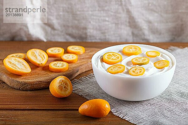 Griechischer Joghurt mit Kumquat Stücken in einem weißen Teller auf einem braunen Holzuntergrund  Nahaufnahme