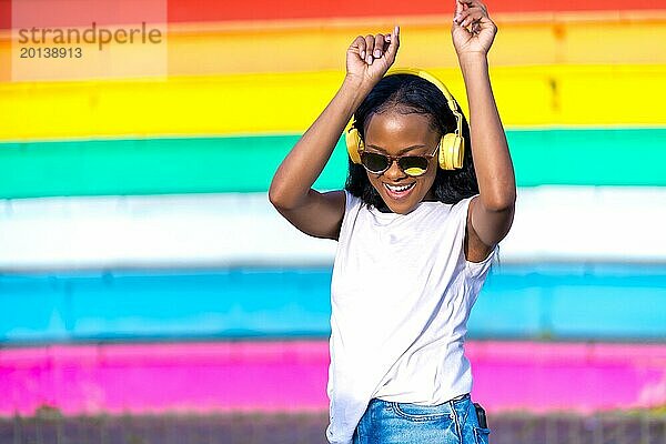 Glückliche und fröhliche afrikanische Frau mit Kopfhörern tanzt in einem Stadtpark