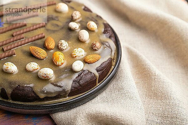 Hausgemachter Schokoladen Brownie Kuchen mit Karamellcreme und Mandeln mit einer Tasse Kaffee auf einem farbigen Holzhintergrund und Leinentuch. Seitenansicht  Nahaufnahme  selektiver Fokus