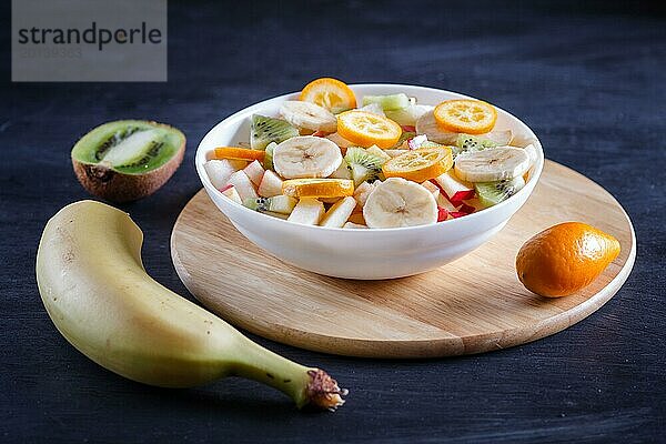 Vegetarischer Salat aus Bananen  Äpfeln  Birnen  Kumquats und Kiwi auf schwarzem woodem Hintergrund  Nahaufnahme  selektiver Fokus