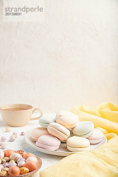 Farbiger Zephir oder Marshmallow mit Kaffeetasse und Dragees auf weißem Betonhintergrund und gelbem Textil. Seitenansicht  Kopierraum  selektiver Fokus