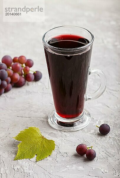 Glas roter Traubensaft auf einem grauen Hintergrund aus Beton. Morninig  Frühling  gesundes Getränk Konzept. Seitenansicht  Nahaufnahme