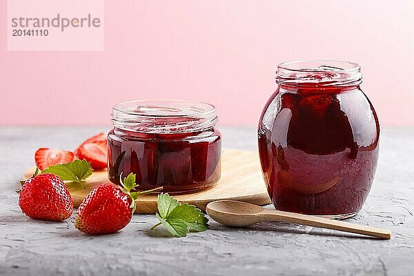 Erdbeermarmelade in einem Glas mit Beeren und Blättern auf grauem Betonhintergrund. Hausgemacht  Nahaufnahme  Seitenansicht  selektiver Fokus