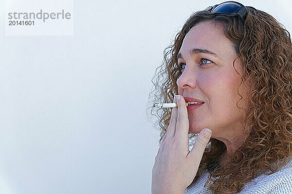 Attraktive blauäugige  gelockte Frau im Profil  die eine Zigarette raucht  mit weißem Hintergrund und Kopierraum