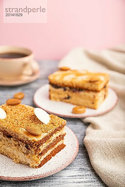 Honigkuchen mit Milchcreme  Karamell  Mandeln und einer Tasse Kaffee auf grauem und rosa Hintergrund und Leinenstoff. Seitenansicht  Nahaufnahme  selektiver Fokus