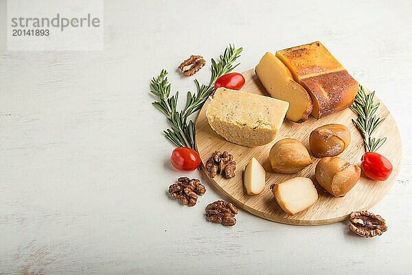 Geräucherter Käse und verschiedene Käsesorten mit Rosmarin und Tomaten auf einem Holzbrett auf einem weißen Holzhintergrund. Seitenansicht  Nahaufnahme  Kopierraum