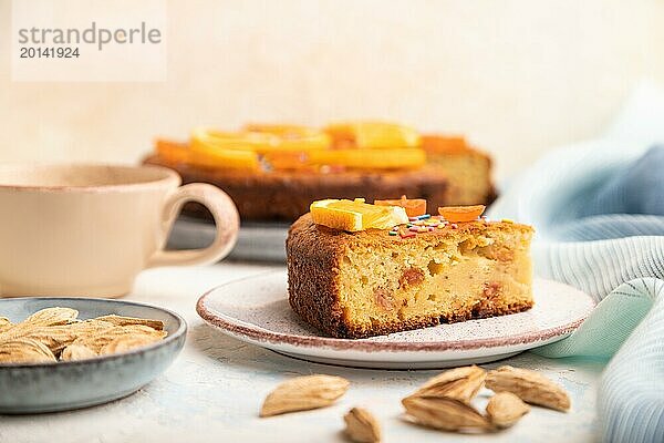 Orangenkuchen mit Mandeln und einer Tasse Kaffee auf einem weißen Betonhintergrund und blauem Leinentuch. Draufsicht  Nahaufnahme  selektiver Fokus