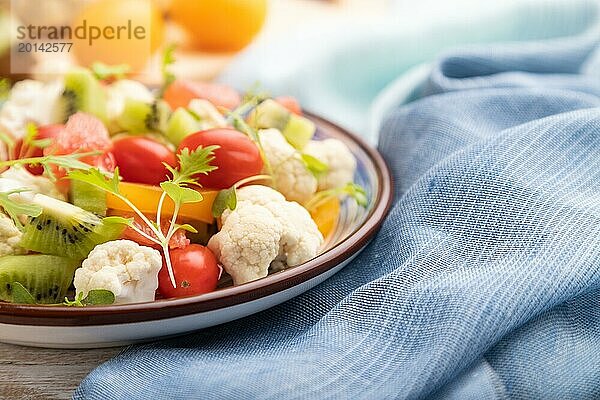 Vegetarischer Salat aus Blumenkohl  Kiwi  Tomaten  Mikrogrünsprossen auf weißem Holzhintergrund und blauem Leinentuch. Seitenansicht  Nahaufnahme  selektiver Fokus