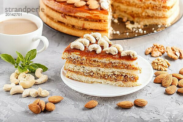 Stück hausgemachter Kuchen mit Karamellcreme und Nüssen mit einer Tasse Kaffee auf einem grauen Betonhintergrund. Seitenansicht  Nahaufnahme  selektiver Fokus