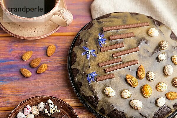 Hausgemachter Schokoladen Brownie Kuchen mit Karamellcreme und Mandeln mit einer Tasse Kaffee auf einem farbigen Holzhintergrund und Leinentuch. Draufsicht  Nahaufnahme  selektiver Fokus