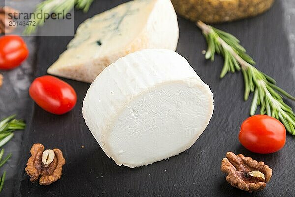 Weißer Ziegenkäse und verschiedene Käsesorten mit Rosmarin und Tomaten auf einer schwarzen Schieferplatte auf einem schwarzen Betonhintergrund. Seitenansicht  Nahaufnahme  selektiver Fokus