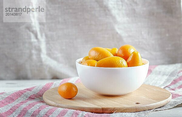 Kumquats in einem weißen Teller auf einem hölzernen Küchenbrett  Nahaufnahme