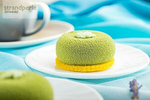 Grüner Mousse Kuchen mit Pistaziencreme und einer Tasse Kaffee auf einem weißen Holzhintergrund und blauem Stoff. Seitenansicht  Nahaufnahme  selektiver Fokus