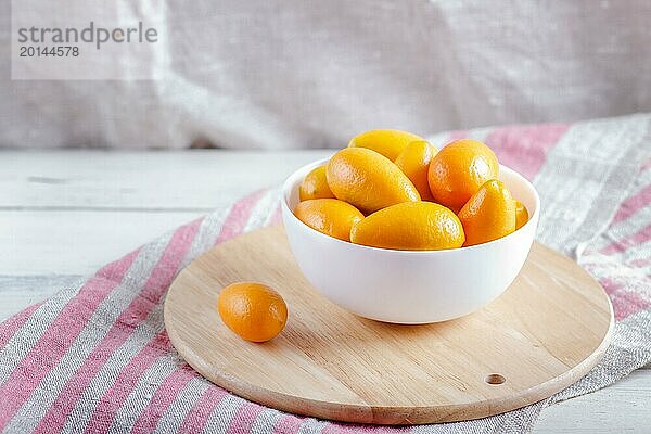 Kumquats in einem weißen Teller auf einem hölzernen Küchenbrett  Nahaufnahme