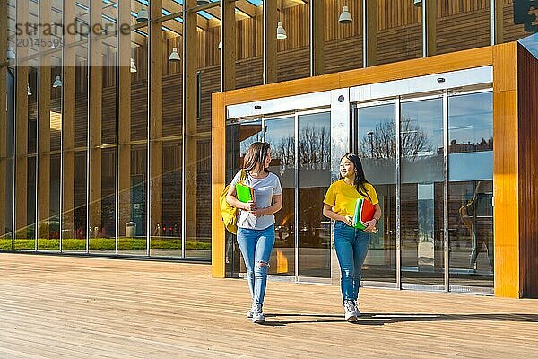 Weite Ansicht mit Kopierraum von zwei Freundinnen  die an einem sonnigen Tag entlang der Universität spazieren gehen