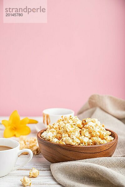 Popcorn mit Karamell in einer Holzschale und eine Tasse Kaffee auf weißem und rosa Hintergrund und Leinenstoff. Seitenansicht  Kopierraum  selektiver Fokus