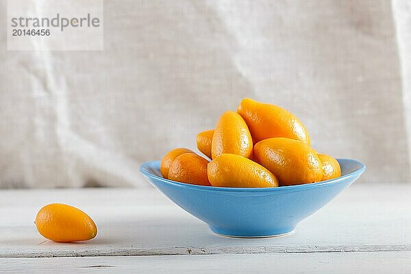 Kumquats in einem blauen Teller auf weißem Holzuntergrund  Nahaufnahme