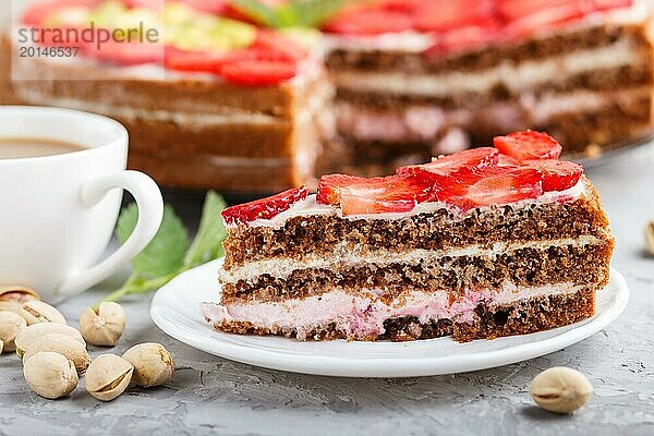 Hausgemachter Kuchen mit Joghurtcreme  Erdbeeren  Pistazien und einer Tasse Kaffee auf einem grauen Betonhintergrund. Seitenansicht  selektiver Fokus  Nahaufnahme